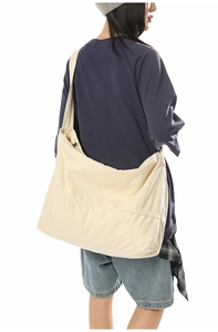 Vue arrière d'un grand sac bandoulière en toile crème porté par un mannequin décontracté