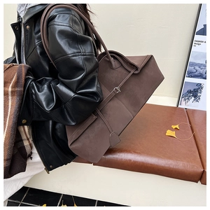 Close-up of a large dark brown suede tote bag with belt detail in an autumn street style