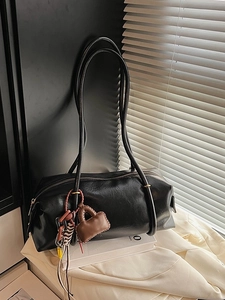 Minimalist black cylinder shoulder bag with side charm pendant on a styled background