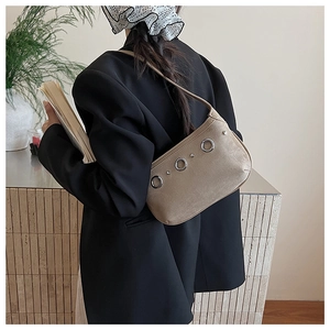Détail des rivets et œillets sur le sac à épaule en daim beige porté par le mannequin