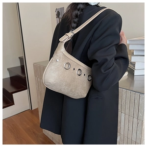 Détail du sac sous l'aisselle en daim beige avec œillets porté sur un blazer noir