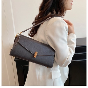 Détail du sac baguette en cuir grainé marron foncé avec fermoir doré sur blazer blanc