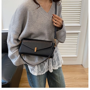 Détail du sac enveloppe noir en cuir grainé avec fermoir doré porté par un mannequin