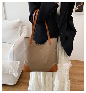 Minimalist khaki nylon tote bag with caramel leather handles held by a model indoors