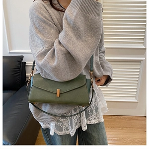 Détail d'un sac bandoulière vert foncé en cuir avec boucle dorée élégante et texture grainée