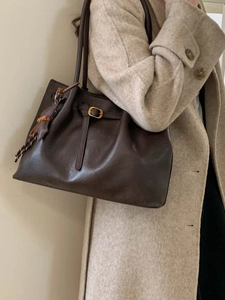 Large brown leather tote bag with gold buckle shown on a model in a beige coat