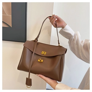 Detail of brown leather tote with dual gold twist-lock closures and long shoulder strap