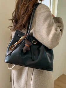 Large black leather tote bag with gold buckle and brown dog charm on beige coat