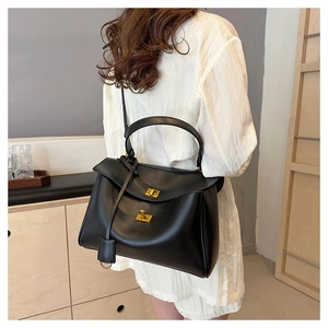 Close-up of minimalist black leather tote bag featuring elegant golden twist lock closures