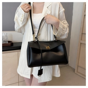 Detail of minimalist black leather tote bag featuring gold metal turn-lock and shoulder strap