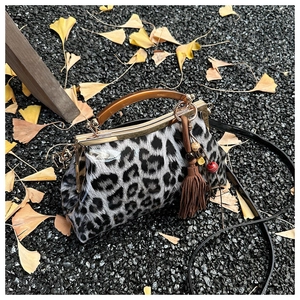 Détail du sac léopard avec fermoir à baiser, poignée ambre et pompon sur feuilles d'automne