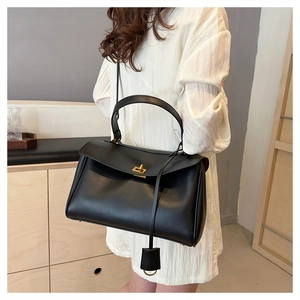 Detail of minimalist black leather tote bag featuring a golden twist lock and slim shoulder strap