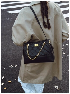 Detail of black quilted shoulder bag with gold chain and metal lock on a khaki trench coat