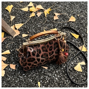 Détail du sac léopard avec poignée en ambre et pompon posé sur des feuilles de ginkgo