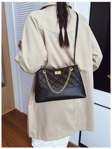 Detail of black quilted crossbody bag with gold twist lock and chain strap on model