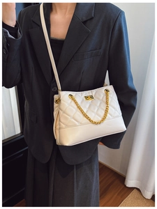 Close-up of quilted cream tote with golden chain and square twist lock on a shoulder strap