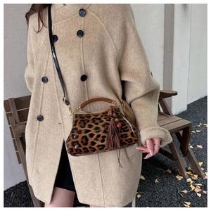 Détail d'un sac léopard avec fermoir doré et pompon porté sur un manteau beige élégant