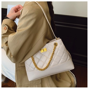 Detail of beige quilted tote bag with gold metal twist lock and chain strap on shoulder