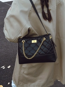 Classic black quilted tote bag with golden twist lock and chain strap on trench coat