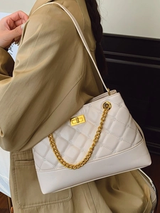 Elegant cream quilted tote bag with gold chain strap worn by a model in a trench coat