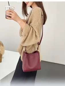Detail of burgundy pebbled leather bucket bag with embossed logo and adjustable strap