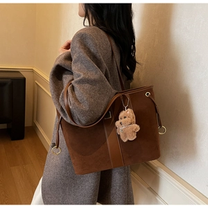 Detail of coffee brown tote bag with metal ring and plush bear charm worn by a model