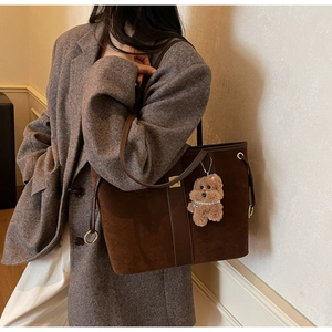 Close-up of deep brown tote bag with suede texture, shoulder strap and plush charm detail