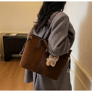 Detail of dark brown suede tote bag with leather trim and plush bear charm on model