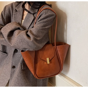 Brown wing-shaped leather tote bag with gold magnetic clasp on tweed blazer shoulder