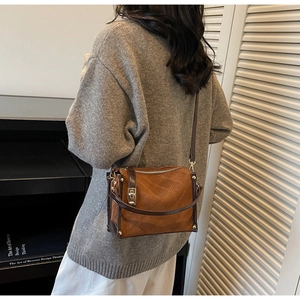 Detail view of brown quilted suede crossbody bag with vintage metal lock on a model