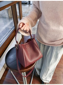 Detail of burgundy pebbled leather bucket bag with folded design and embossed logo