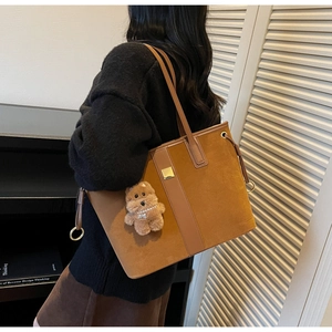 Detail of large brown suede tote bag with leather stripes and cute bear pendant