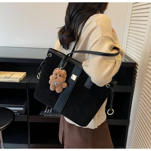 Detail of black suede tote bag with leather straps and brown plush bear charm