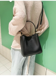 Close-up of black pebble leather bucket bag showing embossed logo and gold metal buckle