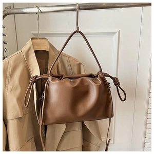 Detail of a brown lychee pattern leather cloud bag hanging on a rack with a trench coat