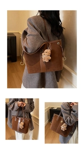 Detail of a brown suede tote bag featuring leather handles and a plush bear pendant charm