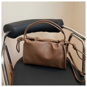 Detail of brown pleated leather cloud bag featuring knot accents and a cylindrical handle