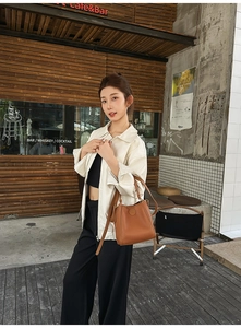 Brown lychee leather bucket bag styled with beige jacket in outdoor street setting