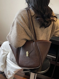 Brown leather shell tote bag with gold buckle shown on shoulder for professional commute