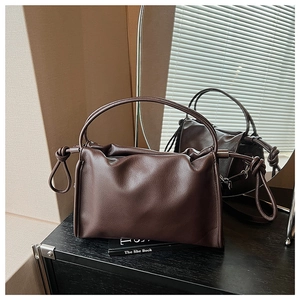 Detail of soft dark brown pleated leather bag with knots on a reflective surface