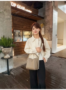Close-up of khaki leather bucket bag with top handle and strap shown in an outdoor setting