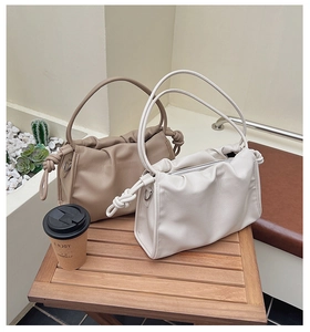 Detail of cream and khaki ruched cloud bags with knotted handles on a wooden table