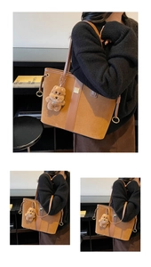 Detail of a large brown suede tote bag featuring a leather strap and a plush bear charm