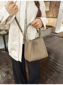 Detail showing the textured pebble leather surface and top handle of a khaki bucket bag