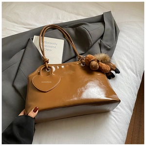 Détail du sac cabas en cuir marron brillant avec breloque peluche sur un costume