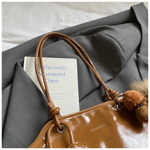 Détail d'un cabas en cuir verni marron avec breloque chien peluche sur blazer gris