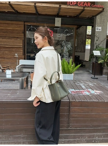 Olive green pebbled leather bucket bag styled with a minimalist outfit in an urban setting