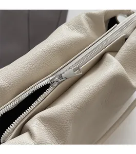 Detailed close-up of smooth silver metal zipper on beige pebbled leather shoulder bag