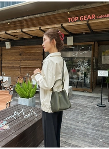 Olive green bucket bag in lychee texture leather held by model in a cozy cafe setting