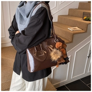 Détail du cabas en cuir verni marron foncé avec poche en cœur et charm en peluche